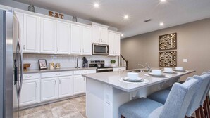 Una cocina moderna con armarios blancos, una isla central con taburetes y un microondas, además de un fregadero.