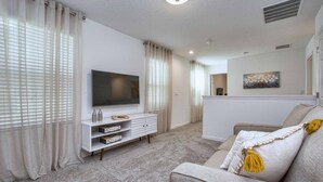 Una sala de estar moderna con un televisor de pantalla plana, un mueble blanco para entretenimiento y un sofá gris con flecos amarillos.