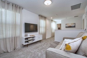 Ein modernes Wohnzimmer mit einem Flachbildfernseher, einer weißen Unterhaltungseinheit und einem grauen Sofa mit gelben Fransen.