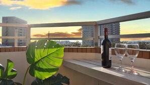 A balcony with a bottle of wine and two glasses, overlooking a cityscape during sunset. - Panoramic Ocean View - downtown/ high speed WiF (Ishigaki)