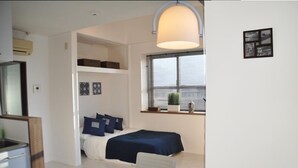 A compact room with a bed, a desk, and a window with blinds. - Panoramic Ocean View - downtown/ high speed WiF (Ishigaki)