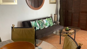 Un salon comprenant un canapé, une table basse en verre, une table ronde en bois et un grand miroir mural.