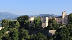 A castle with multiple towers, surrounded by lush greenery and hills in the background.