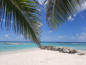 Uma praia com areia branca, águas turquesa cristalinas e um afloramento rochoso.