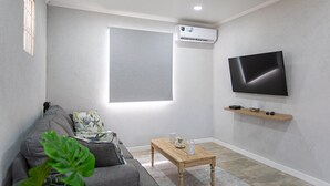 Un soggiorno con un divano grigio, un tavolino in legno, una TV a schermo piatto montata a parete e una piccola mensola sottostante.