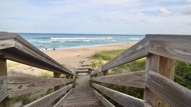 Una scala di legno che conduce a una spiaggia, con una vista limpida sull'oceano e persone in lontananza.