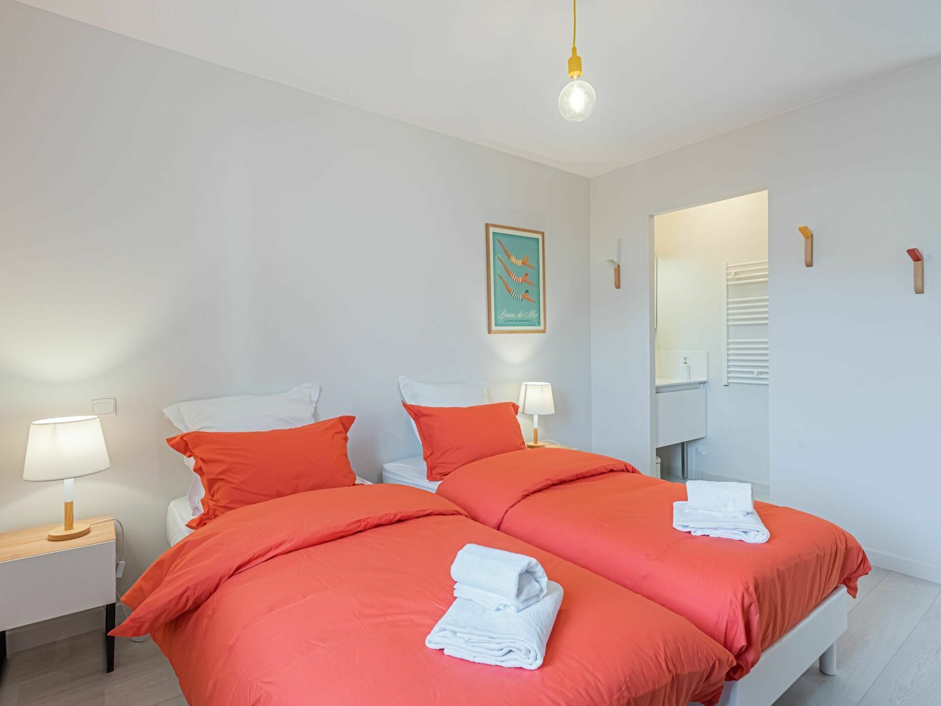 A double bed with orange bedding, two bedside tables with lamps, a wall-mounted mirror, and a framed picture.