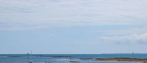 A beach with multiple boats anchored in shallow water, a rocky shoreline, and a clear sky.