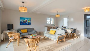 Ein modernes Wohnzimmer mit Sofa, Sesseln, einem Esstisch und einer dahinterliegenden Küchenzeile.