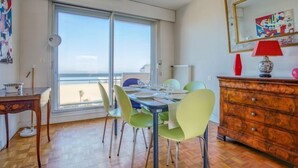 Un coin repas avec une table dressée pour quatre personnes, de grandes fenêtres, une commode et un miroir.