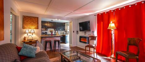 A modern living room with a glass coffee table, a sofa, a red curtain, and a kitchen in the background.