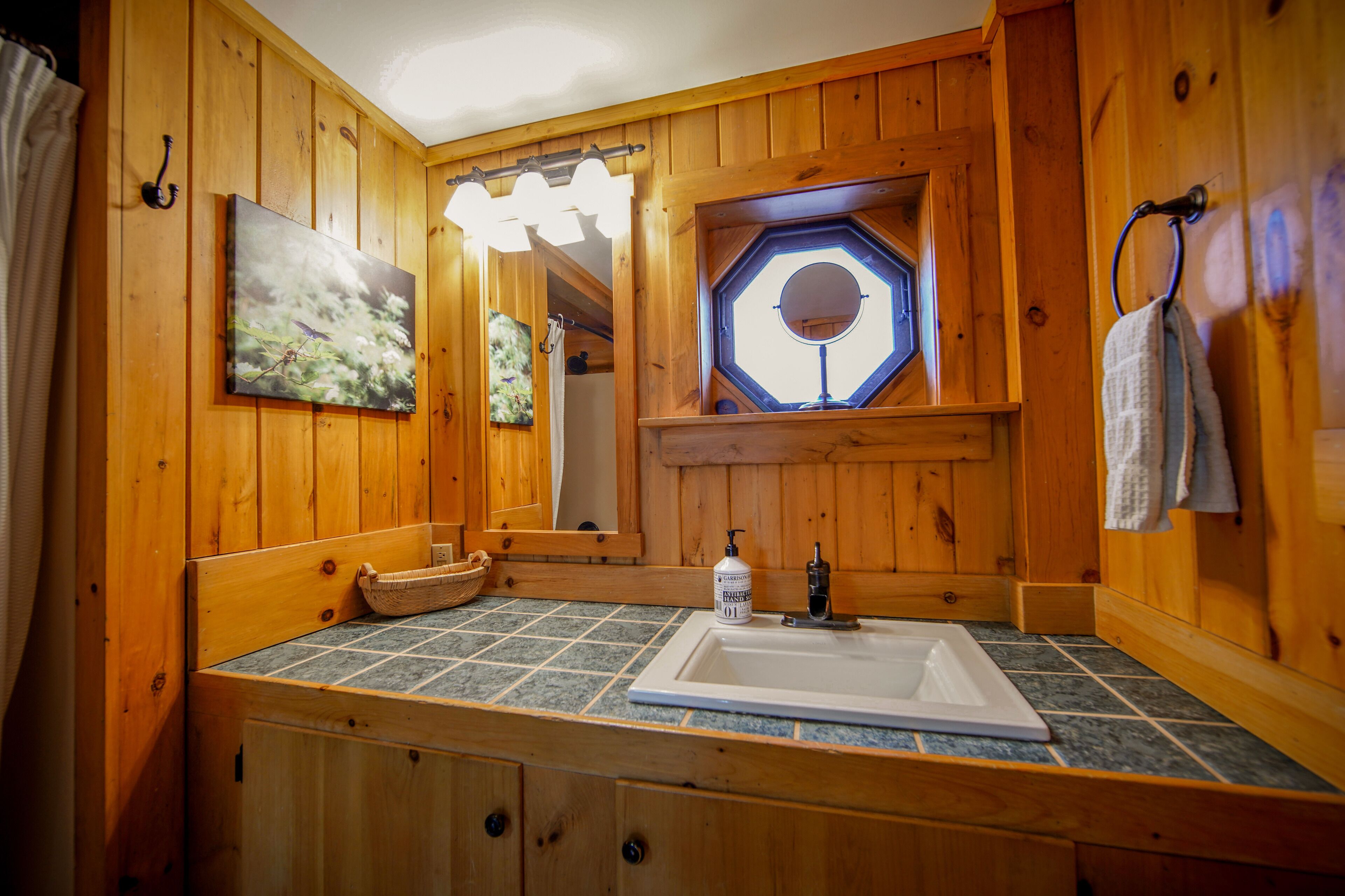 A wooden cabin bathroom with a large mirror, a sink, and a window with a view.
