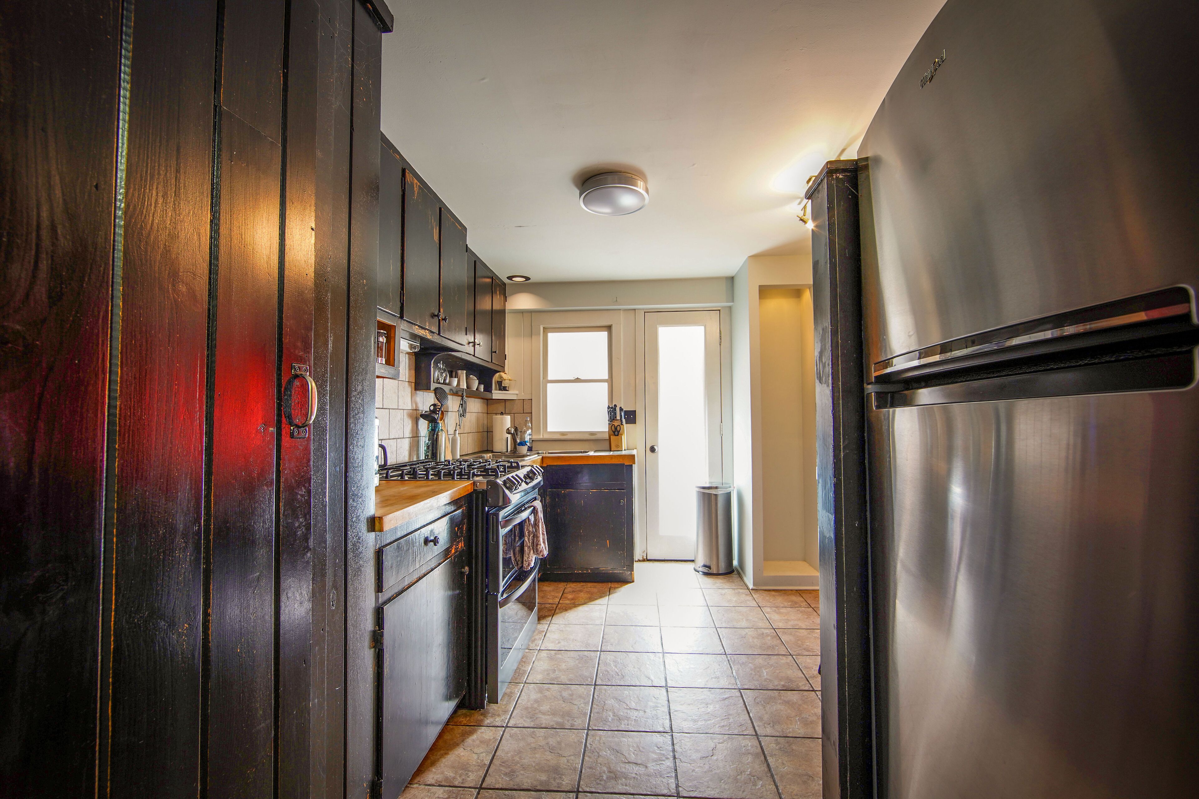 A kitchen with dark wooden cabinets, stainless steel appliances, and a tiled floor.
