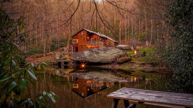 A cabin with a dock and a pond in the foreground.