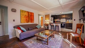 A living room with a sofa, coffee table, and rug. There is a kitchen visible through an open doorway.