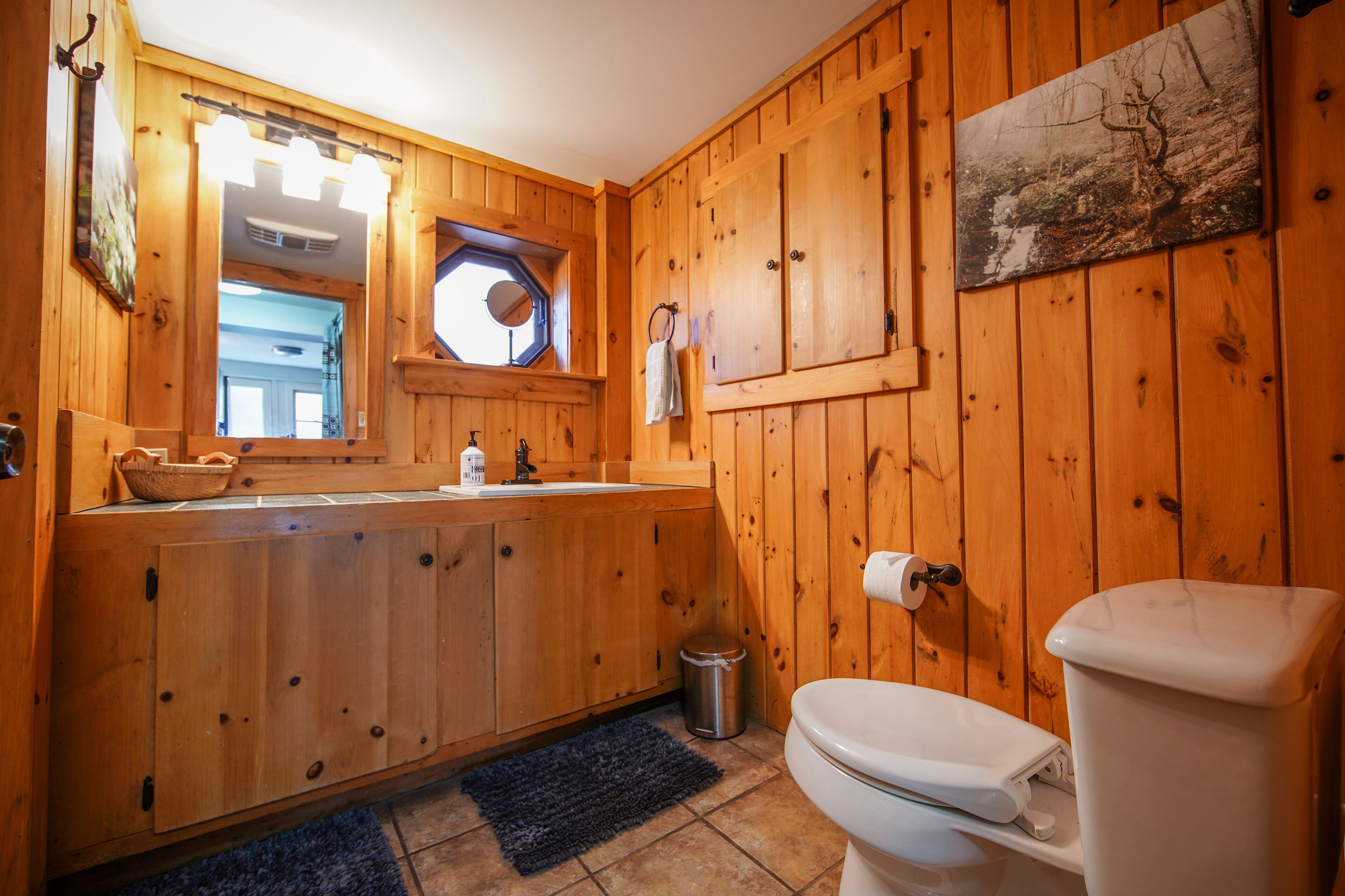 Une salle de bain aux murs lambrissés, équipée d’un lavabo, de toilettes et d’une fenêtre.