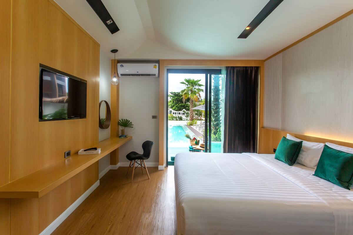 Una camera d'albergo moderna con un letto grande, una TV a schermo piatto, una scrivania con una sedia e vista su una piscina.