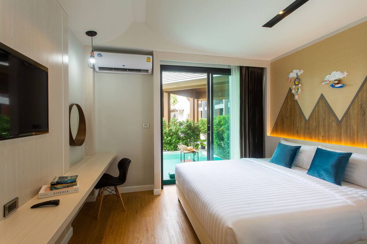 Una camera d'albergo con un letto, una scrivania con una sedia, una TV e un condizionatore d'aria.