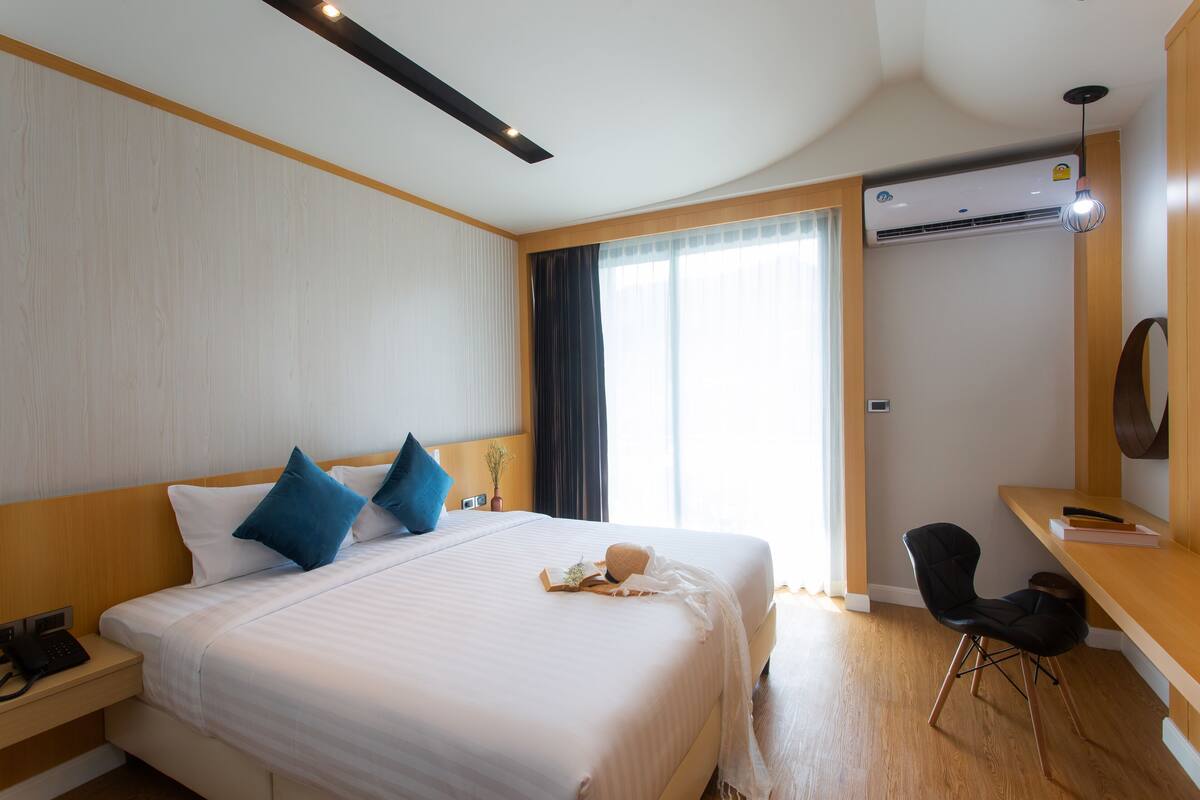 Una camera d'albergo con un letto, comodino, scrivania, sedia e condizionatore d'aria.