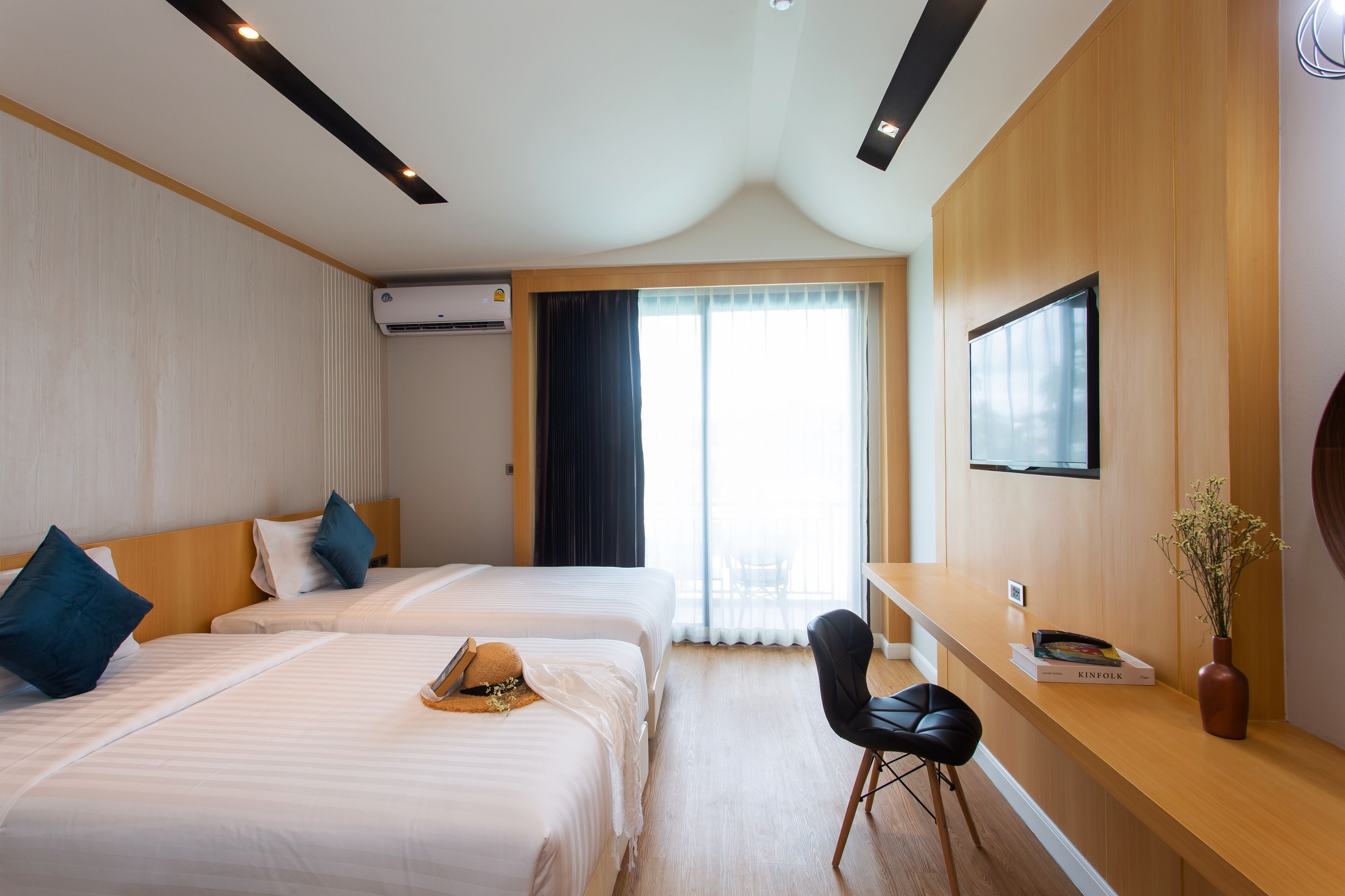 A hotel room with two beds, a desk, a chair, a TV, and a window with curtains.