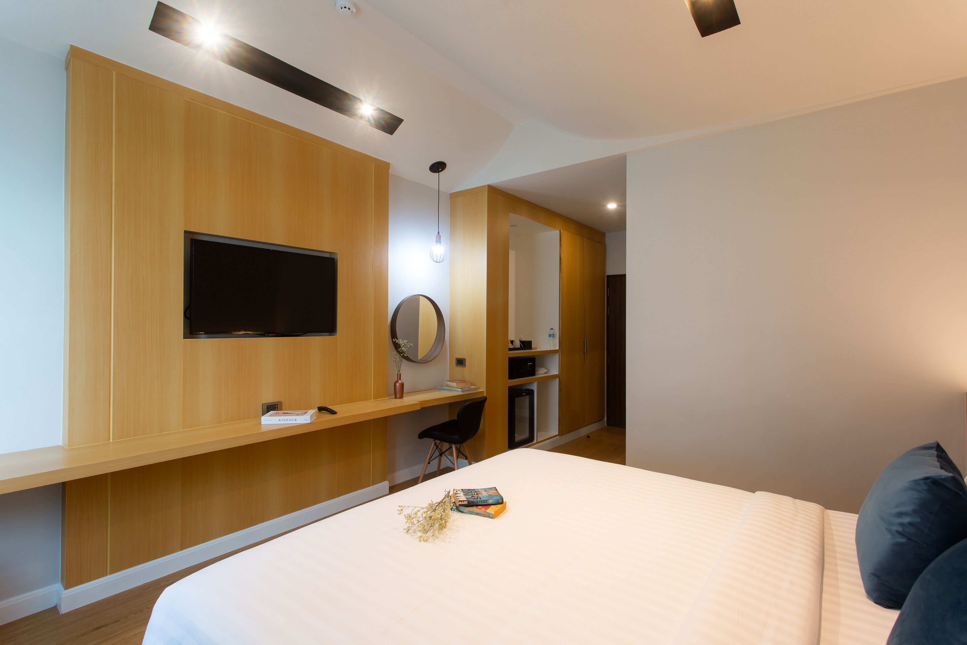 Ein modernes Hotelzimmer mit einem großen Bett, einem Schreibtisch mit Stuhl, einem flachbildfernseher an der Wand und einem kleinen Spiegel.