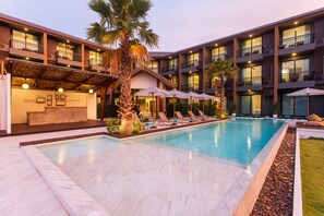 A hotel with a swimming pool, palm trees, and lounge chairs.
