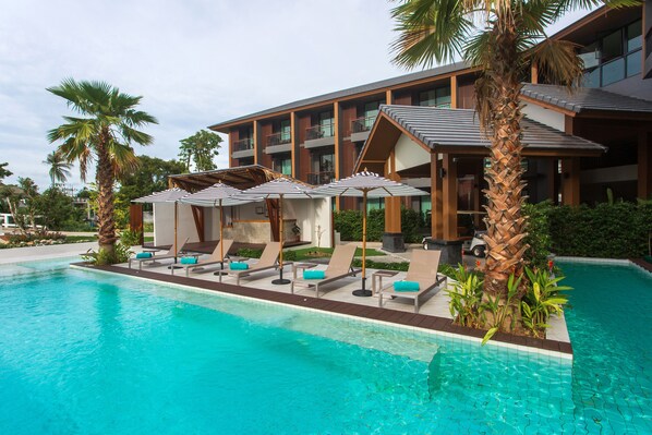 A hotel with a swimming pool, sun loungers, and umbrellas.