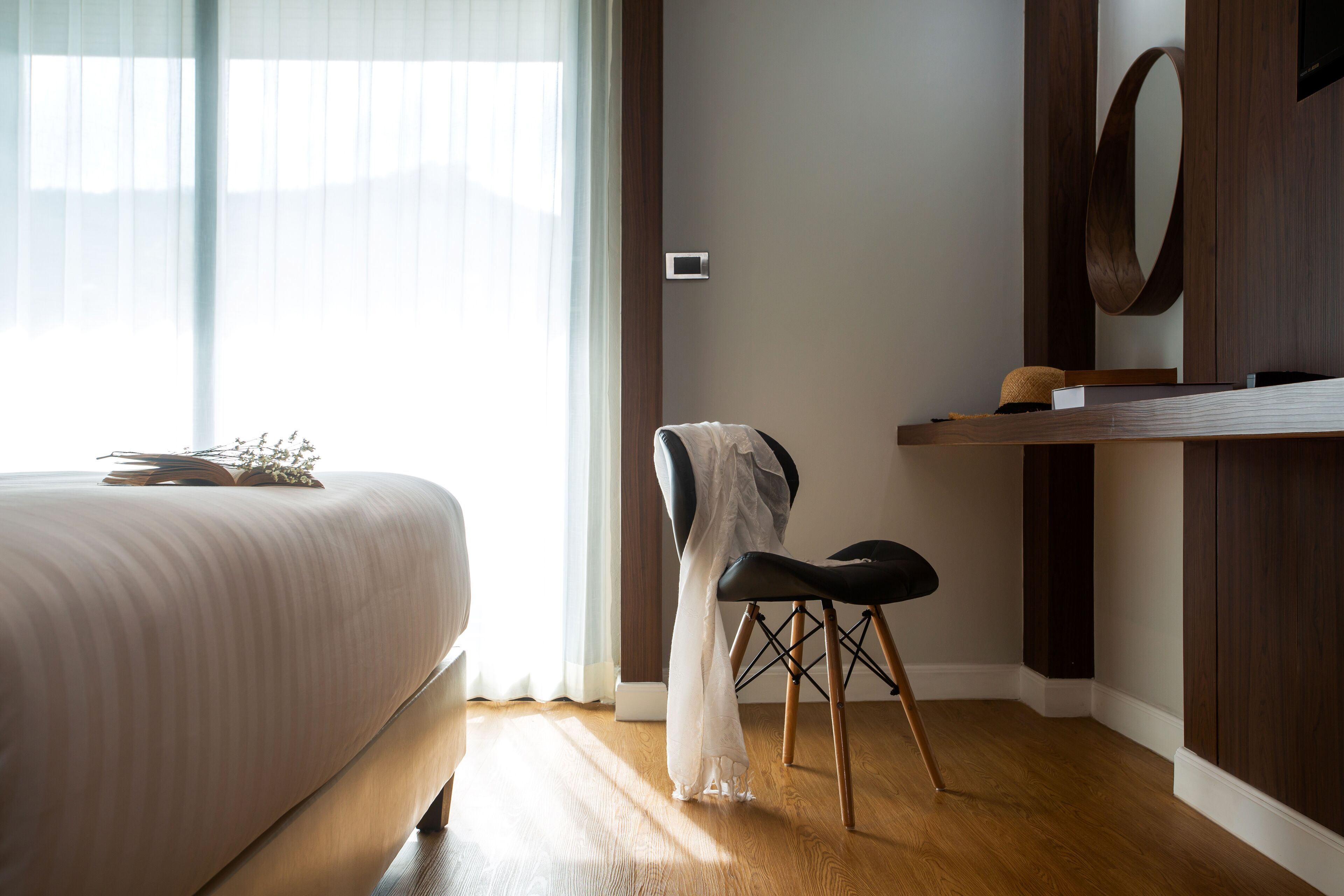 A bedroom with a bed, a chair, a mirror, and a shelf with books and a decorative item.