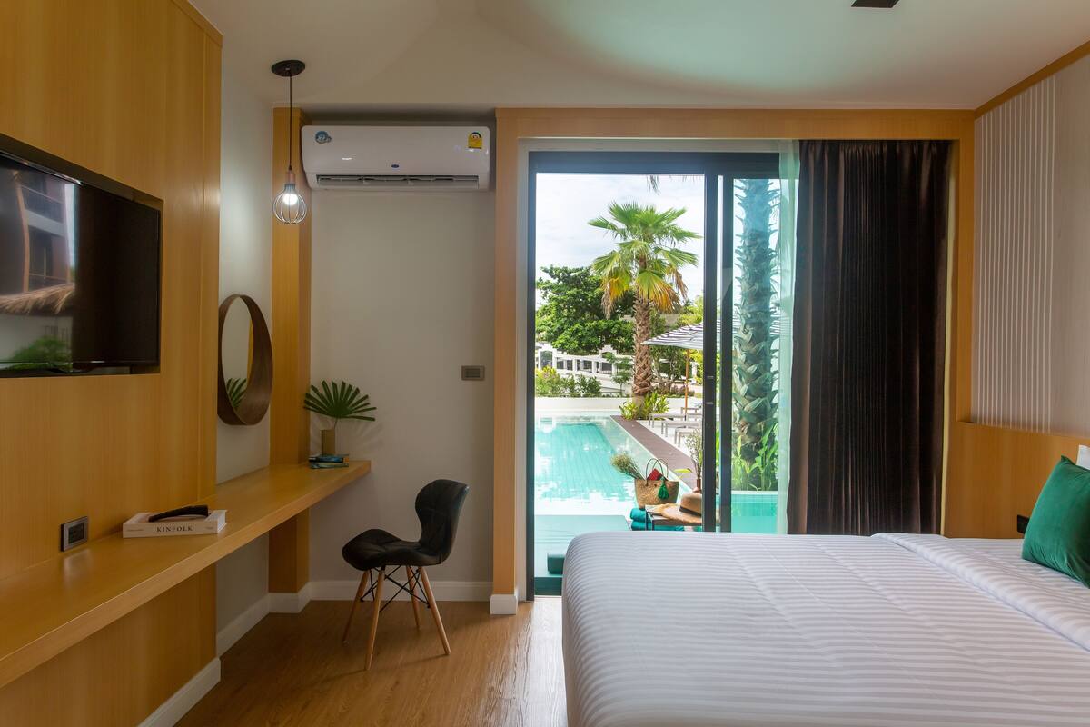 Una camera d'albergo con un letto, una televisione, una scrivania con una sedia, una pianta e vista su una piscina.
