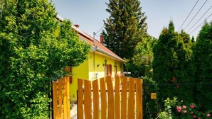 Ein gelbes Haus mit Holzzaun, umgeben von Grünpflanzen und Bäumen.