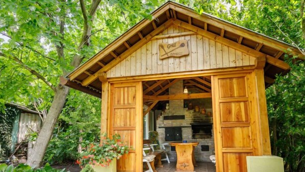 Eine Holzhütte mit großer offener Tür, einem Steinkamin und einem Esstisch mit Stühlen vor der Hütte.