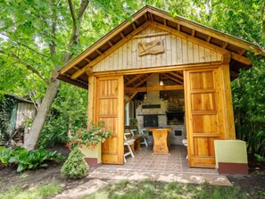 Una cabana de fusta amb una porta gran oberta, una llar de pedra i una taula de dinar amb cadires a l'exterior.