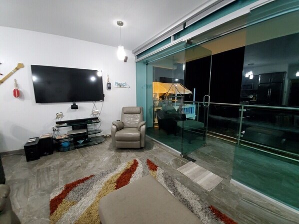 A modern living room with a flat-screen TV, a leather chair, and a glass door leading to a balcony.