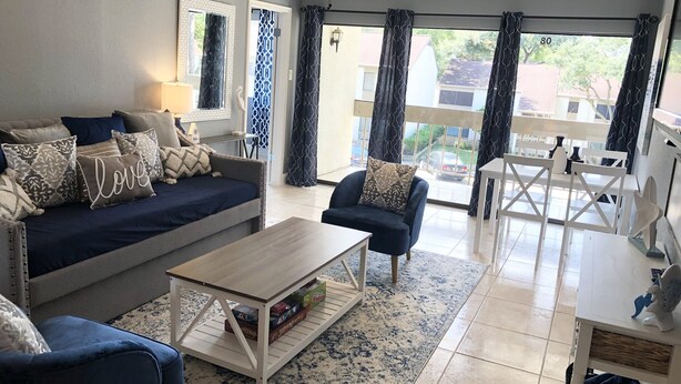 Un salon moderne avec un canapé, un fauteuil et une table basse, un balcon doté d’une balustrade et offrant une vue sur l’extérieur.