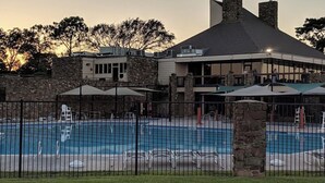 Un espace piscine avec des chaises longues et des parasols, un mur en pierre et un bâtiment doté d’une cheminée.