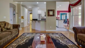 A spacious living room with a wooden coffee table, a patterned rug, and a sofa. A kitchen area is visible in the background. - Ridge Creek Getaway, ideal 4 Friends&Family get-togethers, events & receptions.  (Brentwood)
