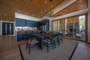 A modern kitchen with dark cabinets, a large dining table, and a stone fireplace.