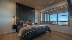 A modern bedroom with a large bed, wooden ceiling, and a view of the outdoors through large windows. - Capstone - Aska Adventure Area (Blue Ridge)