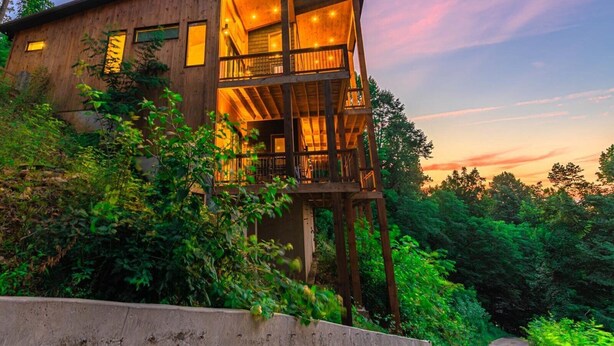 A modern wooden house with multiple levels and large windows, surrounded by lush greenery. - Capstone - Aska Adventure Area (Blue Ridge)