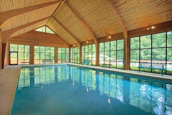 An indoor swimming pool with wooden beams, large windows, and a bench along the side.