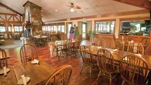 Un restaurant avec des tables et des chaises en bois, une cheminée en pierre et de grandes fenêtres.