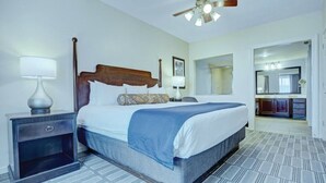 A hotel room with a large bed, a nightstand, a ceiling fan, a bathroom visible through an open door, and a patterned floor. - Alexandria | Couples Capital Stay | Gym + WiFi (Alexandria)