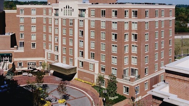 A multi-story brick building with a central courtyard, outdoor seating, and a landscaped area. - Alexandria | Couples Capital Stay | Gym + WiFi (Alexandria)