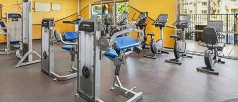Een fitnessruimte met cardioapparatuur, krachttrainingsmachines en een spiegelwand.