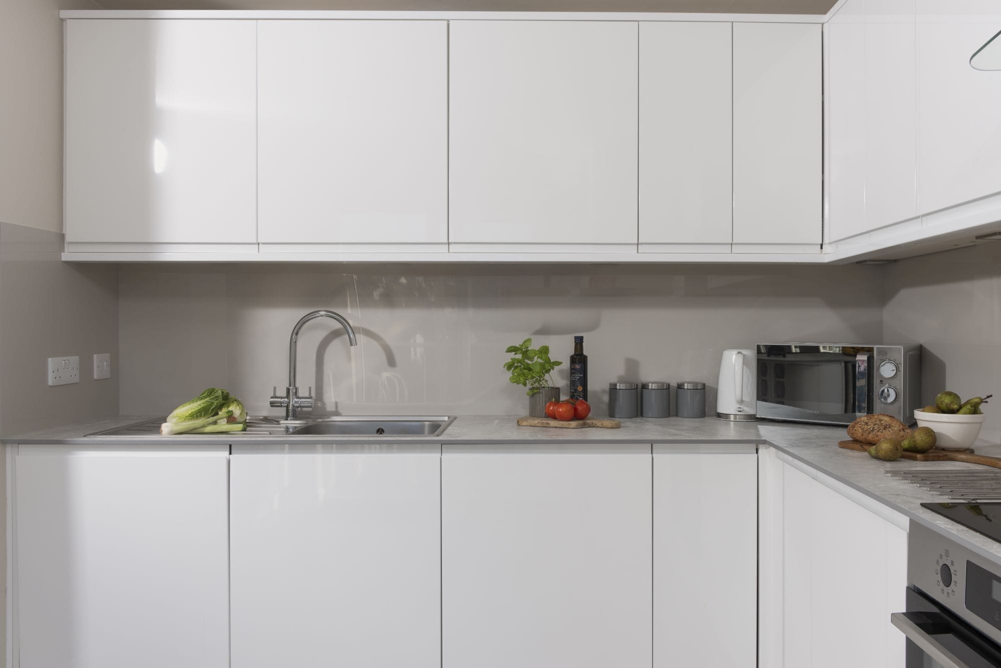 A modern kitchen with white cabinets, a stainless steel sink, a microwave, and a stove.
