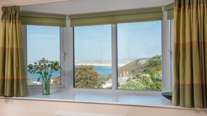 Habitación con ventana saliente que da a un paisaje costero, radiador debajo de la ventana y un florero con flores en el alféizar.