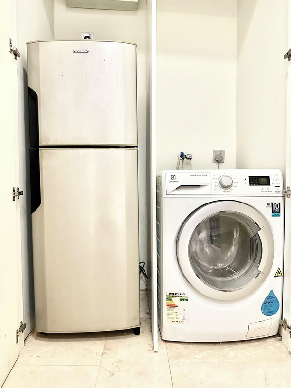 A compact kitchenette with a refrigerator and a front-loading washing machine.