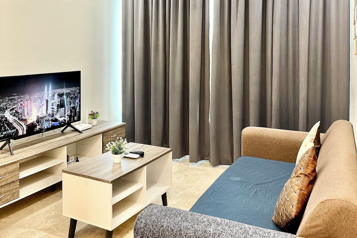 A modern living room with a flat-screen TV, a sofa, a coffee table, and a large window with curtains.