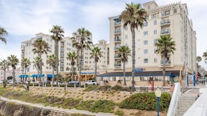 Un hotel de varios pisos con balcones, palmeras y una playa en primer plano.