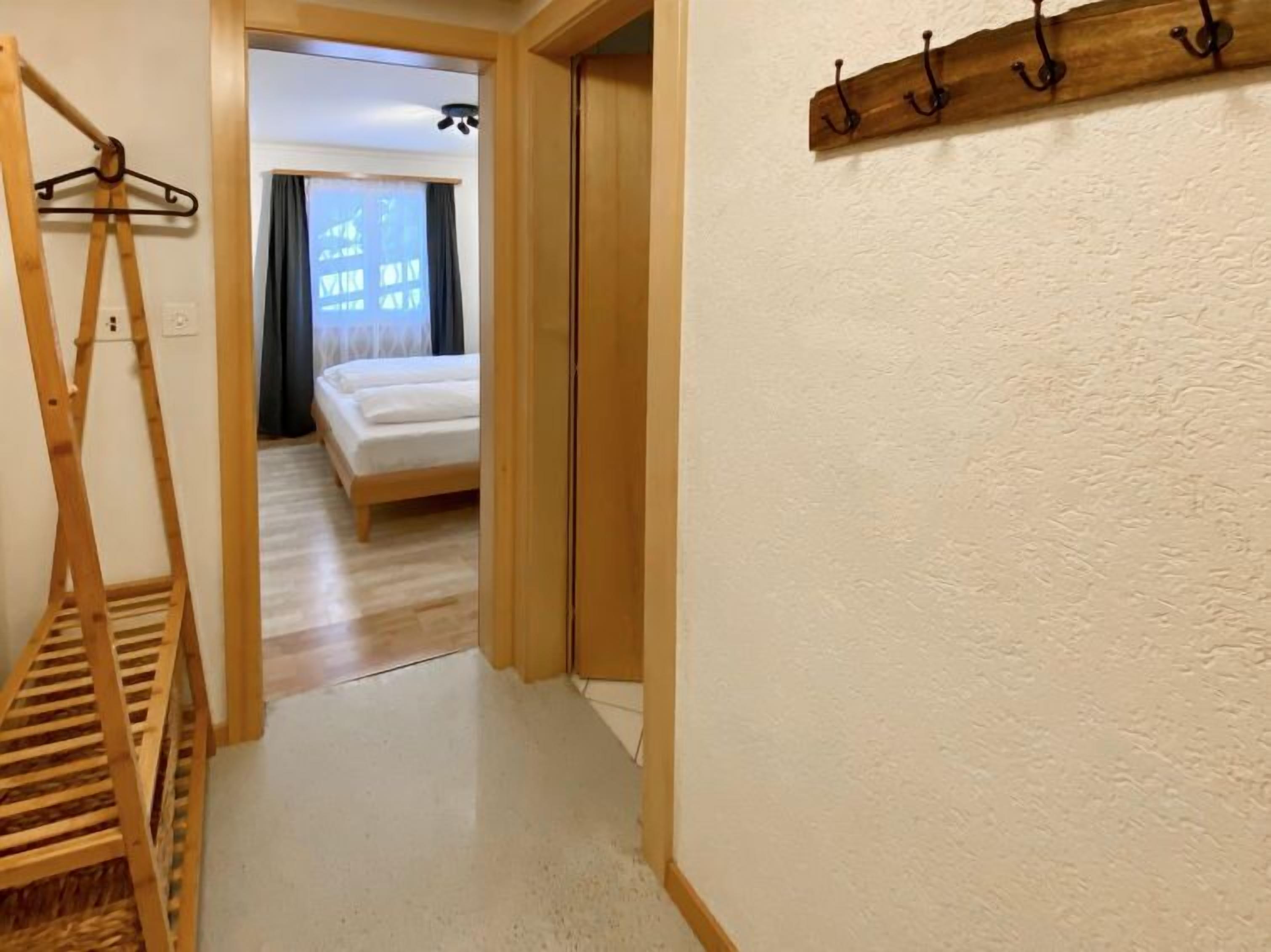A hallway leading to a bedroom with a bed, a wooden coat rack, and a ceiling fan.